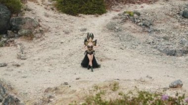 Uzun sarı örgüleri ve siyah elbisesi olan koyu renkli bir kraliçe kayalık ve volkanik bir arazide güçlü bir şekilde poz veriyor. Geniş açı onun fantezi dünyasının destansı ve ıssız güzelliğini yakalar..