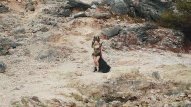 Yüksek açılı bir izleme çekimi siyah elbiseli bir kraliçeyi izler, uzun sarı örgüleri, ıssız bir volkanik kanyona doğru yürürken onu takip eder. Sahne destansı, yalnız ve fantezi hikayeleriyle dolu..