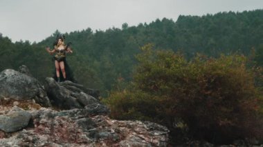 Siyah elbiseli bir cadı ve taç yeşil ağaçlarla dolu bir dağda bir kayanın üzerinde dans ediyor.