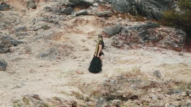日中に岩だらけの山の火口を歩く黒いドレスのゴシック様式の女性 — ストック動画