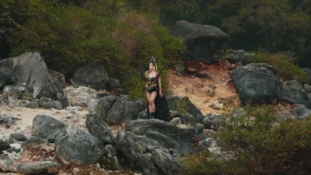 緑の木々に囲まれた山の岩の上で黒のガウンと王冠の魔女が踊る — ストック動画
