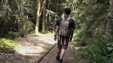Asyalı bir adam gün boyunca ormanda bir patikada yürüyor.
