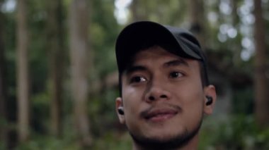 Asyalı bir adam sabahın erken saatlerinde yeşil ağaçlarla dolu bir ormanda gökyüzüne bakıyor.