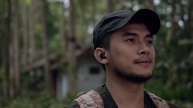 Asyalı bir adam sabahın erken saatlerinde yeşil ağaçlarla dolu bir ormanda gökyüzüne bakıyor.