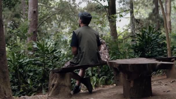 Азиат Черной Шляпе Сидит Деревянном Стуле Наслаждаясь Пейзажем Посреди Леса — стоковое видео
