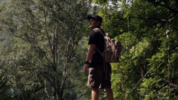 日中森の中の美しい自然景観を眺めながら崖の端に立つアジア系の男 — ストック動画