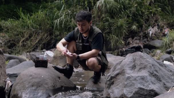 森の中の大きな岩の間の川の水で顔を洗っているアジアの男 — ストック動画