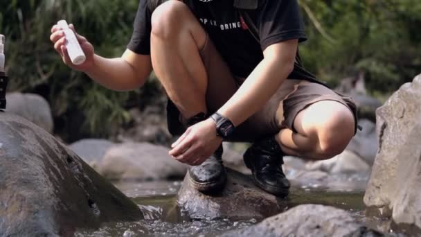 黒いシャツを着たアジア系の男が朝森の中の川で顔を洗っている — ストック動画