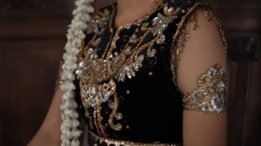 Gelinin elbisesinin ayrıntıları bir kadının vücudunda altın, siyah ve turuncu renkte.