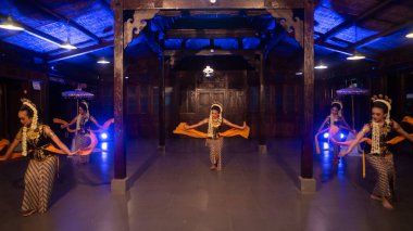 Sarı kostümlü bir grup Sundanyalı dansçı gece mavi ışığın önünde geleneksel bir dans ediyorlar.