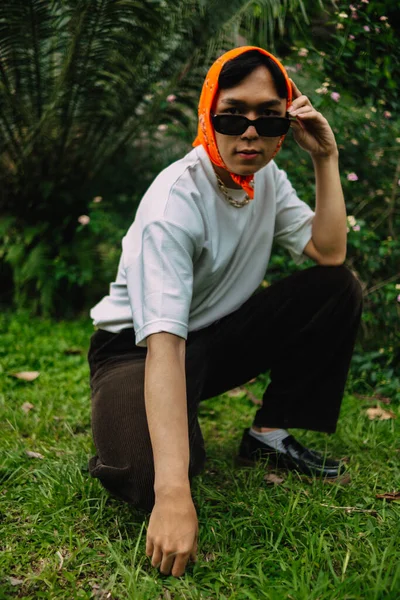 stock image a teenage boy is sitting in sunglasses and an orange bandana in a park full of green grass