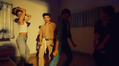 Asyalı bir grup adam renkli ışıklarla dolu bir odada arkadaşlarıyla dans ediyor.