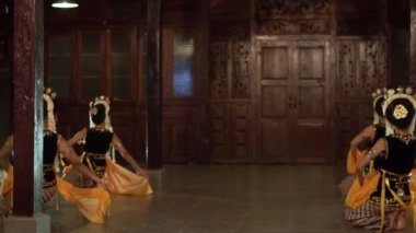 Sarı şallı bir grup Balili dansçı bir binada arkadaşlarıyla yavaşça dans ediyor.