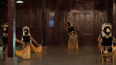 Sarı şallı bir grup Balili dansçı bir binada arkadaşlarıyla yavaşça dans ediyor.