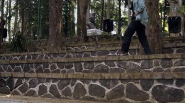 Kot ceketli Asyalı bir kadın sabahın erken saatlerinde ormanın ortasındaki bir parkta terasta oturuyor.