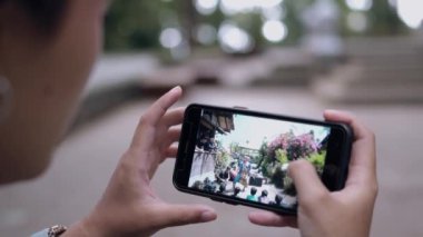 Asyalı bir kadın sabah kafede otururken elinde akıllı bir telefona bakıyor.