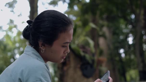 一个亚洲女人坐在咖啡店里 手里拿着智能手机 看着手机 — 图库视频影像