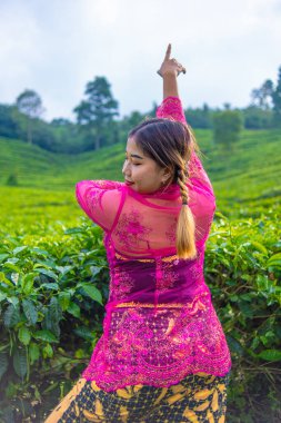 Pembe kostümlü Asyalı bir kadın sabah çay tarlasının önünde poz veriyor.