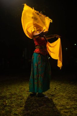 Geleneksel bir Endonezyalı dansçı, geceleri havada süzülen sarı bir eşarpla dans eder.
