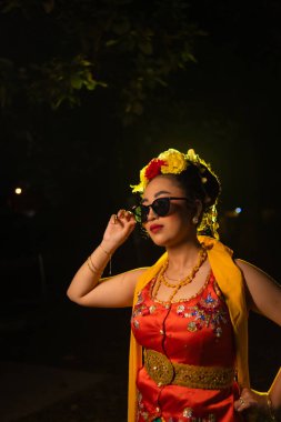 Geceleri güneş gözlüğü takarken çok güzel el hareketleriyle dans eden geleneksel bir Java dansçısının portresi.