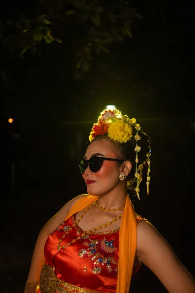一位身着橙色服装 头戴太阳镜 头戴鲜花的桑德拉舞蹈家 穿着一身橙色服装 在耀眼的灯光前摆姿势 — 图库照片