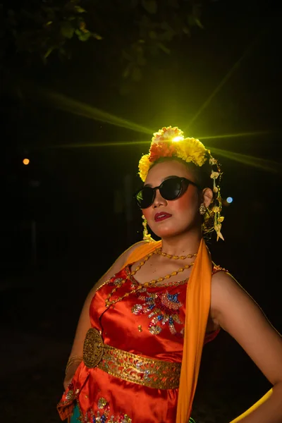 一位身着橙色服装 头戴太阳镜 头戴鲜花的桑德拉舞蹈家 穿着一身橙色服装 在耀眼的灯光前摆姿势 — 图库照片
