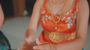 Ellerine kelepçe takıp, süslü turuncu kostümler, makyaj ve çiçekli başlıklar içinde iki gülümseyen Java dansçısını ortaya çıkarmak için eğilmek, gece hazırlanırken birlikte gülmek..