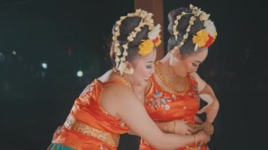 Biri diğerinin performansından önce geleneksel bir Endonezya dans kostümüne karmaşık, pırıl pırıl bir altın kemer takmasına yardım ederken, iki kadının ellerinin yakın plan çekimi..