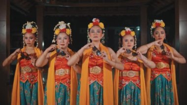 Geleneksel kostüm ve başlık giymiş beş kadın Cava dansçısından oluşan bir grup, geceleri aynı anda güneş gözlüğü takıp ciddi bir ifade takıyorlar..