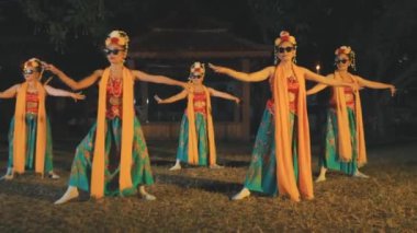 Geleneksel giyimli ve güneş gözlüklü beş Java dansçısının geceleri çimenlerde senkronize bir gösteri sergiledikleri geniş bir çekim. Arka planda geleneksel bir Java pavyonu ve yangın meşaleleri görülüyor.