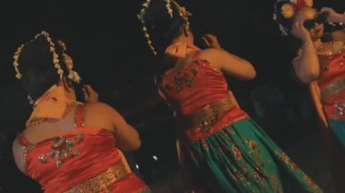 Bir grup geleneksel Cava dansçısı gece arkadaşlarıyla güneş gözlüğü ve turuncu kostümler içinde dans ediyorlar.