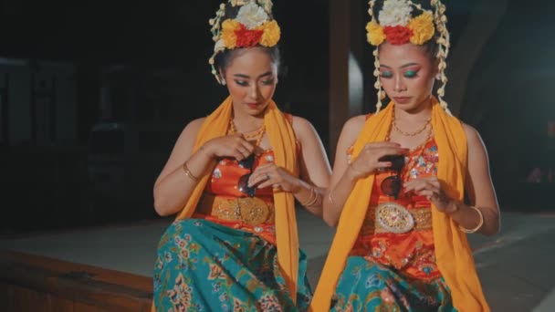 Пара Индонезийских Танцовщиц Оранжевых Костюмах Сидят Своими Друзьями Павильоне Ночью — стоковое видео