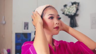 Dramatik göz makyajı ve kırmızı dudaklı genç bir kadın yumuşak saç bandını takar, yüzünü ve at kuyruğunu kontrol eder. Hazırlanıyor ya da güzellik rutinini bitiriyor.