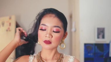 Dramatik makyajı, altın küpeleri ve kolyesi olan güzel bir kadın uzun siyah saçlarını klipsten indiriyor ve kendine güvenerek şekillendiriyor. Güzellik ve moda konsepti.