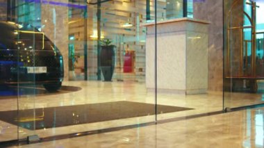 Modern, lüks bir otel lobisinde çantasıyla rahatça yürürken şık bir kadının bacaklarını takip eden düşük açılı bir çekim..