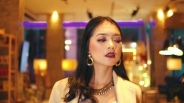 Makyajlı ve şık giyinmiş bir kadının gece vakti lüks, aydınlık bir otel lobisinde rahatça poz verişini izlemek..