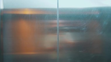 Kapanırken yansıtıcı metalik asansör kapılarına bakan bir bakış açısı. Yüzeyde görünen sıcak iç ışıkların soyut yansımaları.