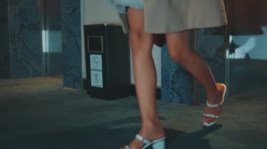 Düşük açılı takip çekimi beyaz topuklu bir kadının bacaklarını ve kısa bir elbiseyi takip ederek halı kaplı bir koridorda güvenle yürürken..