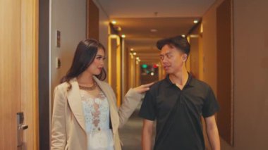 Zarif bir elbise ve ceket giymiş genç, güzel bir Asyalı kadın yanından geçmeden önce elini bir erkeğin omzuna koyar. Lüks bir otel koridorunda güvenle yürüyor ve onu geride bırakıyor..