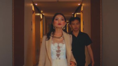 Şık giyimli Asyalı bir kadın lüks bir otel koridorunda güvenle yürürken, onu bir erkek takip ediyor. Çantasını yeşil elbiseli bir asistana uzatır ve bir başkası için ceketini çıkarır..