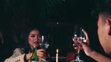 Bir çiftin ellerinin kadeh kaldırarak kadeh tokuşturduğu romantik bir gece randevusu sırasında bir masada mumun üzerinde kadeh kaldırdığı bir sahne..