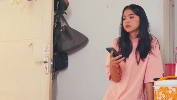 Asijská Žena Vypadá Ztracen Myšlenkách Zatímco Drží Smartphone Ruce Místnosti — Stock video