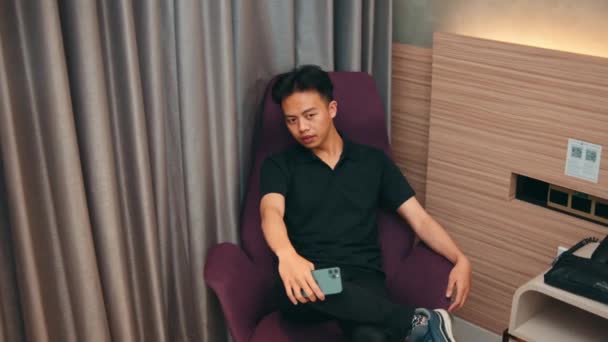 아시아 사람은 방에서 여친을 기다리는 자주색 소파에 앉아있다 — 비디오