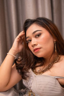 Asyalı bir kadın, akşam partisinde erkek arkadaşını beklerken yüzüne parti elbisesi ve makyaj yaparken güzel bir şekilde oturuyor.