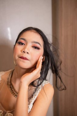 Beyaz elbiseli ve siyah saçlı Asyalı bir kadın gece otel odasında seksi ve zarif poz veriyor.