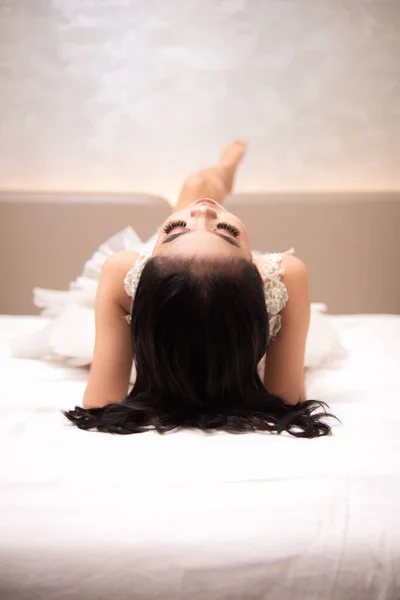 an Asian woman with black hair is sleeping on a white bed in an elegant hotel at night