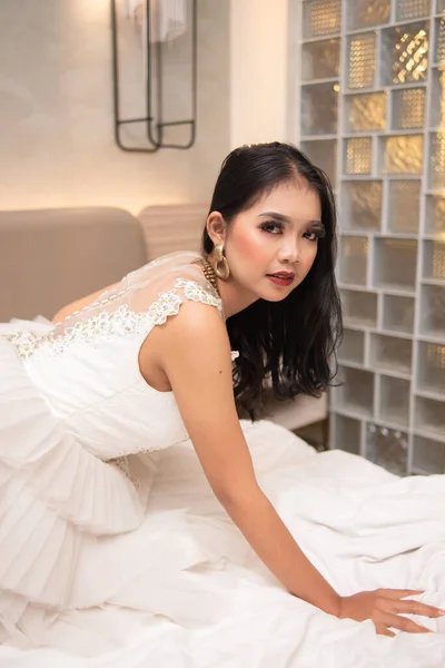白いドレスのアジアの女性は夜に白いベッドで馬鹿に見える顔でセクシーなポーズをしています — ストック写真