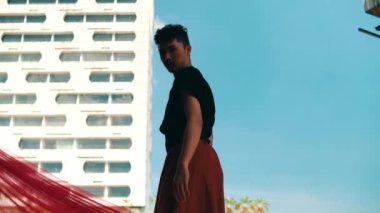 Asyalı bir adam, mavi gökyüzü ve gün boyunca uçan kırmızı bir bezle binanın önünde duruyor.