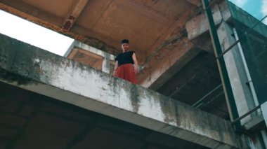 Bir binanın beton kenarında duran Asyalı bir adam güpegündüz yüksek bir yerden aşağıya bakıyor.