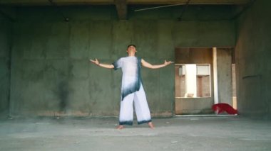 Asyalı bir adam, eski bir binada gün boyunca beyaz elbiseler giyerken vücudundaki kumaşı çözer.